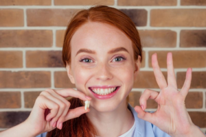 Woman holding up her extracted wisdom tooth and smiling